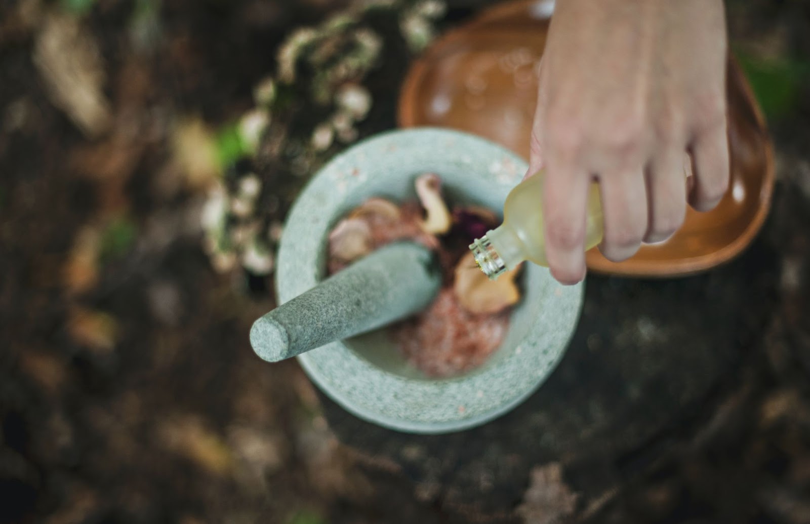 Mixing fresh and extracted herbs for hair health with a mortar and pestle. 