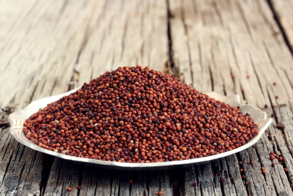 Indian superfoods finger millet red hued in shallow bowl on wood table.