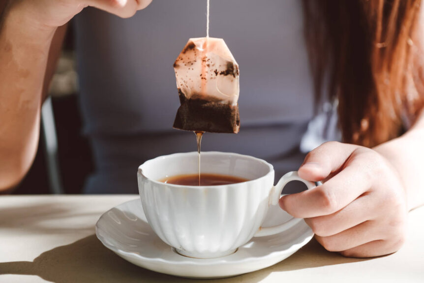 Woman holding teabag above a white tea cup.