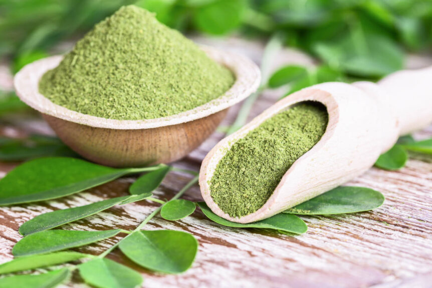 Moringa super green powder on wooden table with leaves.