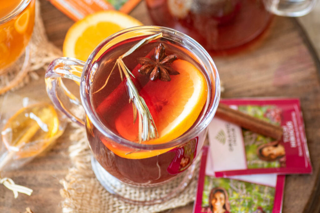 Tulsi Hibiscus Mulled Tea with cinnamon and orange in clear tea mug.  