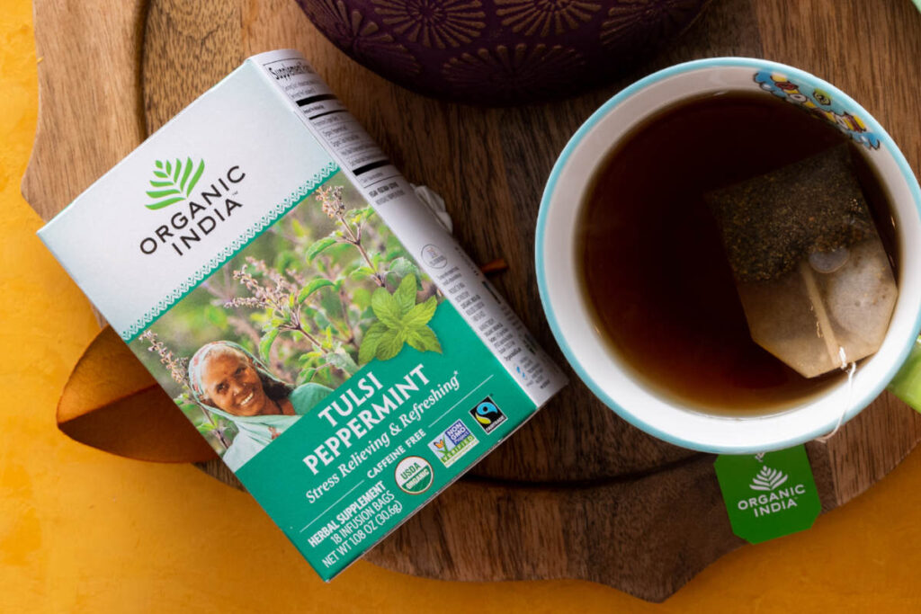 Non-GMO, Fairtrade Tulsi Peppermint Tea box beside a cup of tea. 
