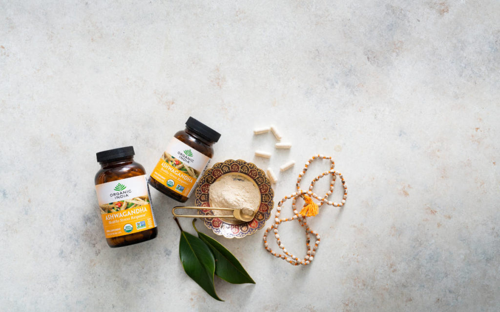 Ashwagandha powder and capsules on a marble counter with a mala necklace.