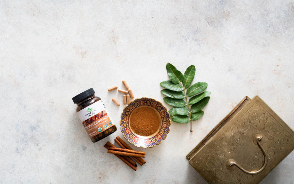 Ceylon Cinnamon powder and capsules on a marble counter with gold bowls, leaves and cinnamon sticks. 