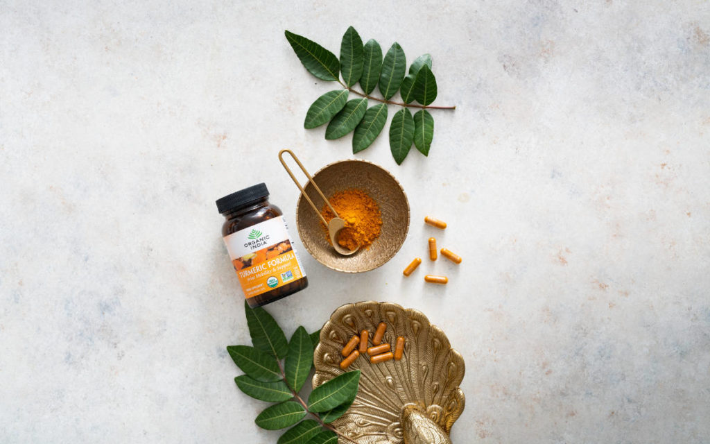 Turmeric powder and capsules on a marble counter with gold bowls, one of the 7 Organic India favorites.