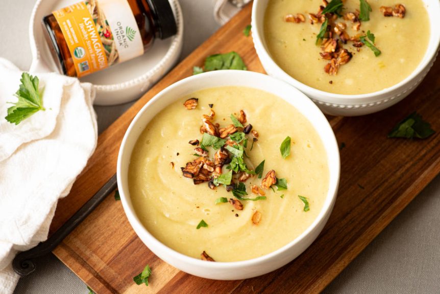 Potato leek soup with parsley garnish in white bowl on wooden cutting board.