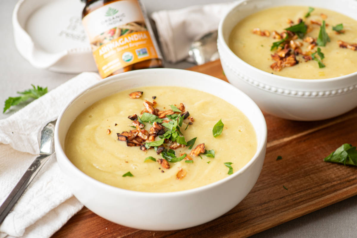 Potato leek soup with parsley and tempeh topping in white bowl on wooden cutting board.