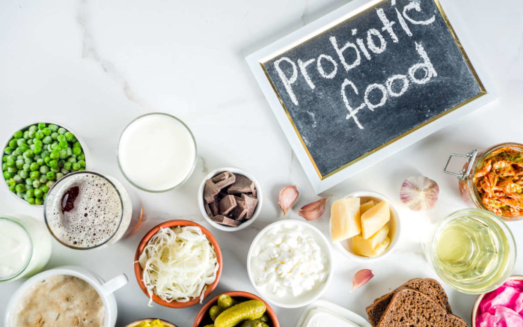 Probiotic foods like yogurt, kombucha, soft cheese, and pickles in bowls on a marble table. 