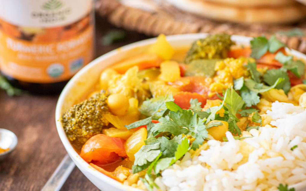 A bowl half filled with rice and other half with 1-pot pumpkin curry with veggies.