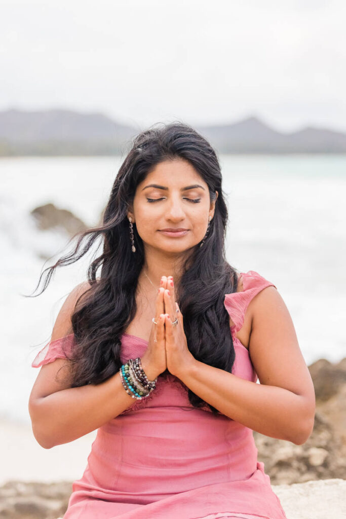 Radhika Mukhija, Women's Coach and Mentor, with hands in prayer position by a lake.