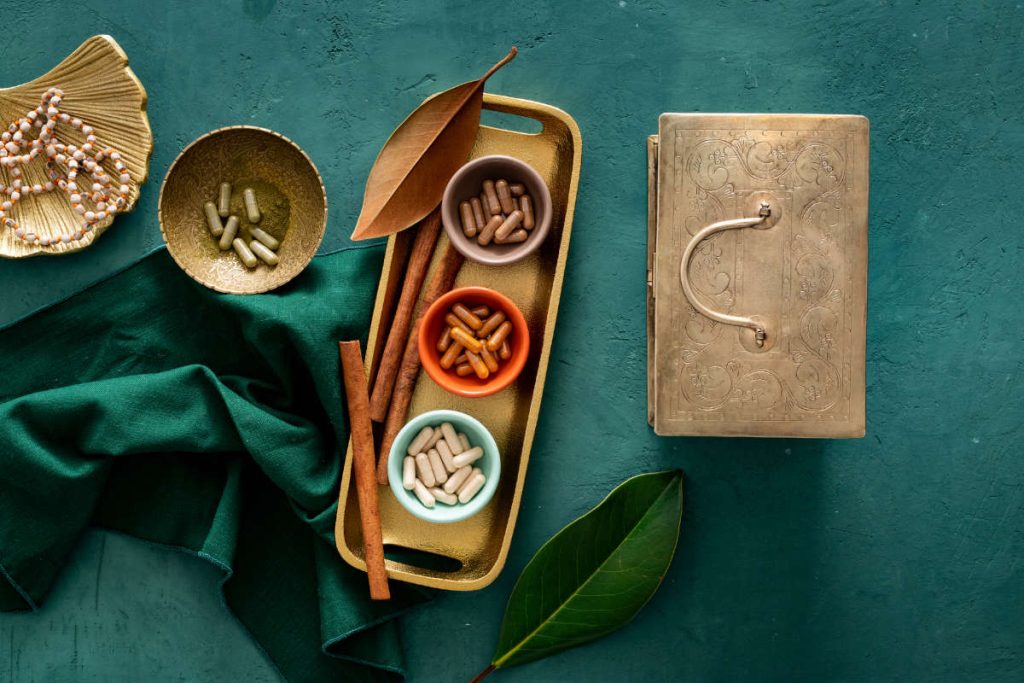 Rasayana herbs capsules in individual little bowls on crushed green velvet table with meditation mala. 