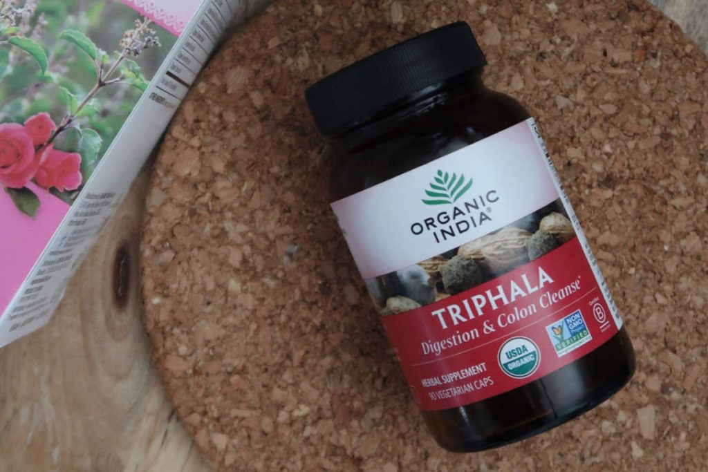 Triphala rasayana herb capsules in dark amber glass jar on cork table 