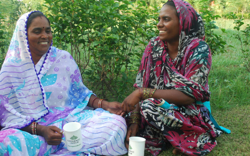 Two women in a green garden in India enjoying Organic India fairtrade tea.
