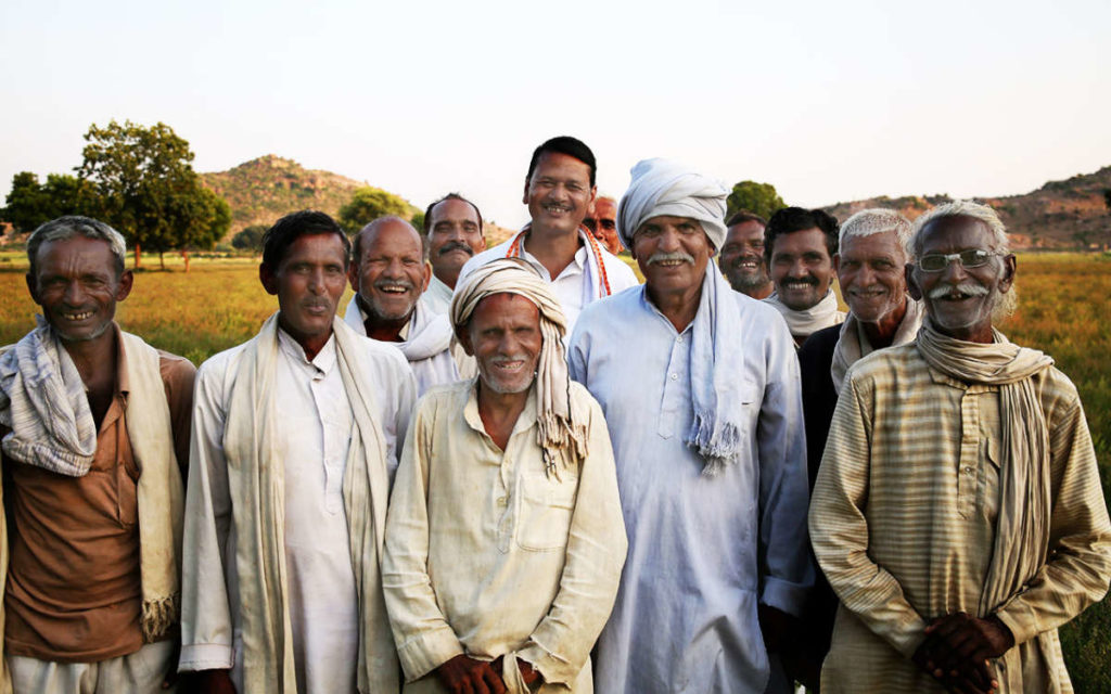 Group of 12 men farmers together smiling in front of a Fairtrade farm.