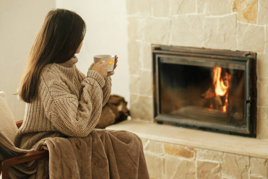 Woman practicing self nurturing by drinking tea in cozy sweater by a fireplace