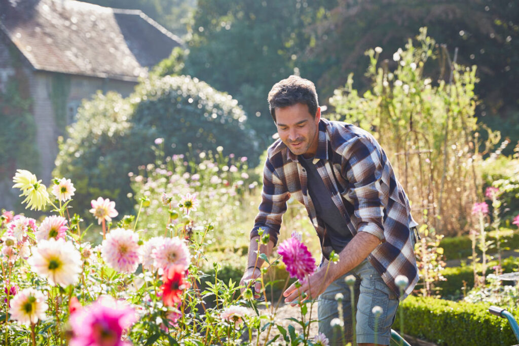 Man practicing self nurturing by gardening and planting flowers in a garden.