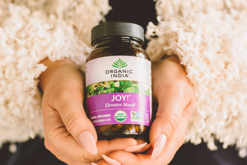 Woman with fluffy jacket holding Joy! Mood capsules, containing shankhpushpi, in her hands.