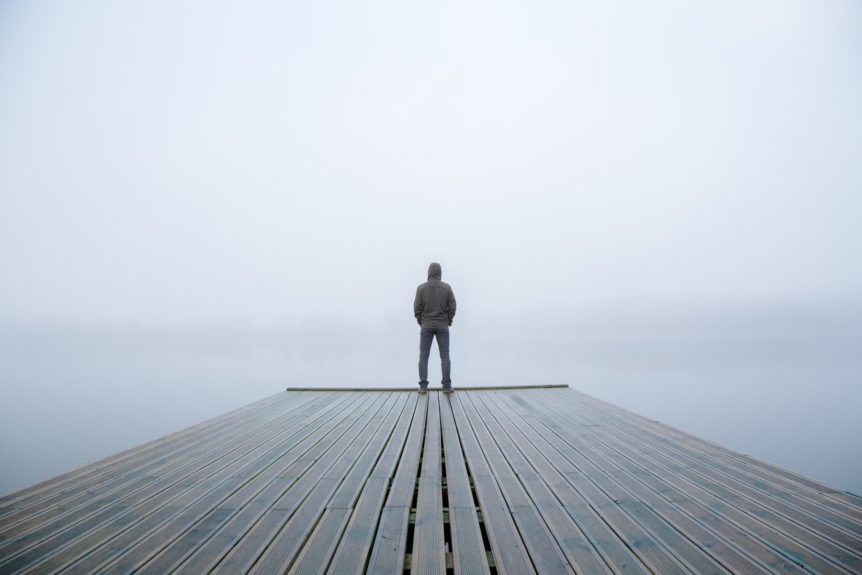 Man standing and reflecting in the power of silence on a foggy pier.