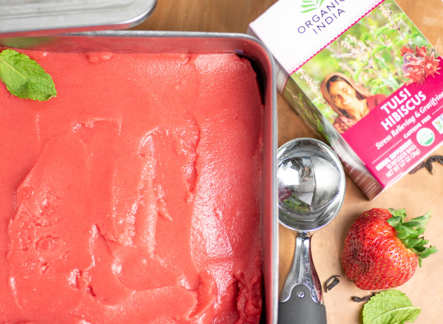 Delicious tulsi hibiscus sorbet freshly frozen in a silver pan with fresh strawberries.