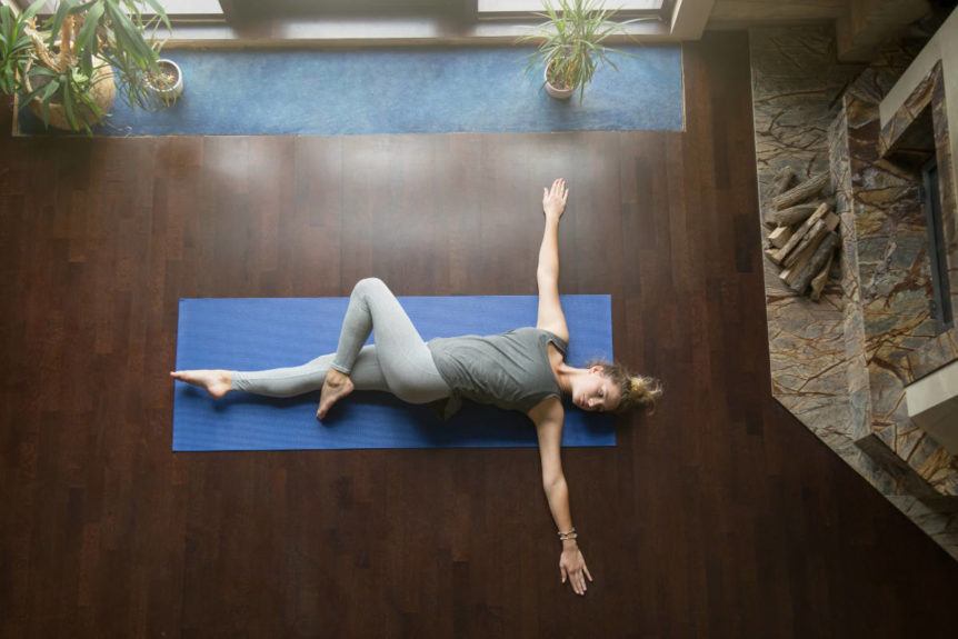 Supine twist on blue mat at home doing yoga poses for digestion.