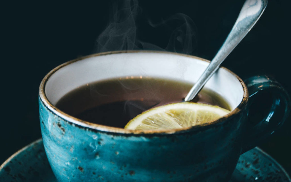 A blue teacup of hot tea with a lemon garnish and silver spoon. 