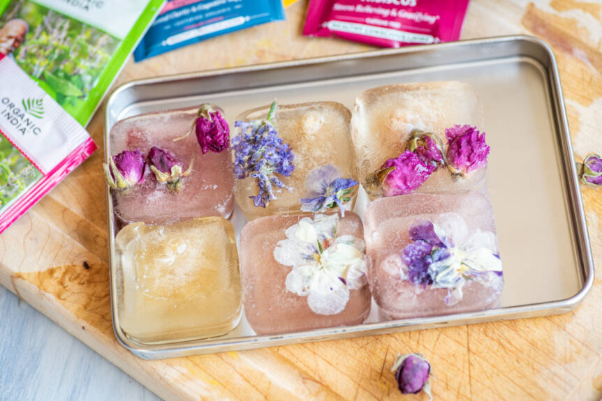 Tea ice cubes in silver tray with floral garnishes frozen inside