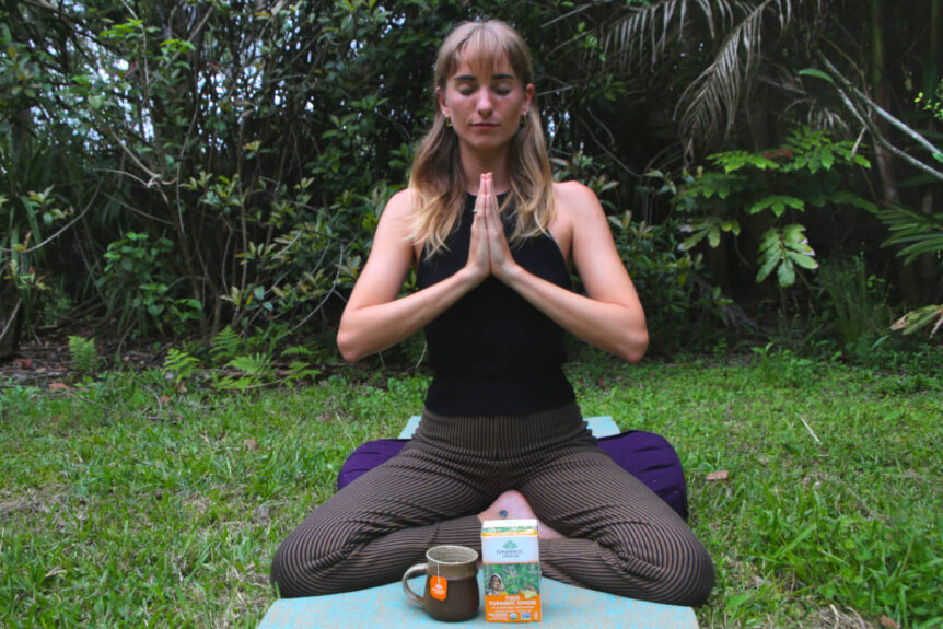 Woman sitting in meditation with tea on a yoga mat outside in nature