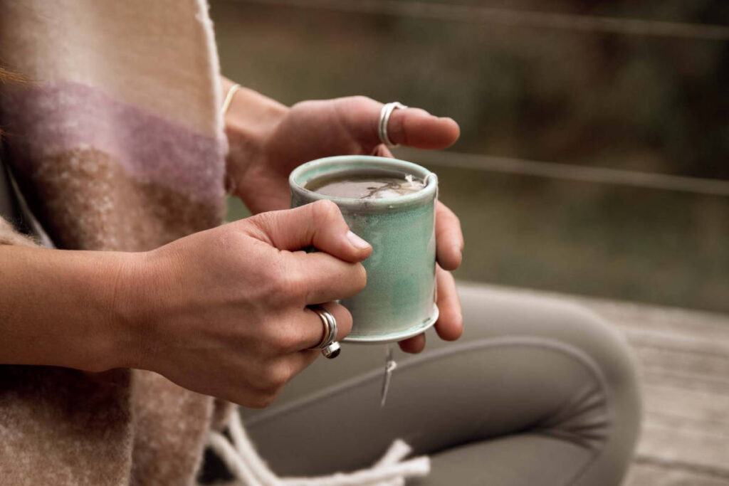 Women with silver rings holding a teal mug for a tea meditation 