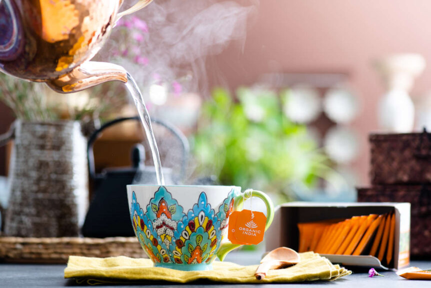 tea ritual pouring tea into colorful mug from copper pot.