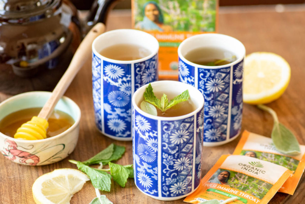 Soothing throat tea in blue and white floral pattern cups with lemon and honey on cutting board. 