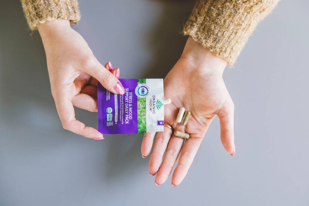 Stress and Mood Support Daily Pack Capsules Purple Pack pouring into woman's hand.