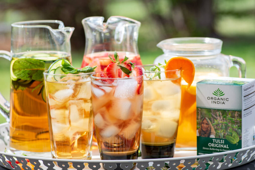tulsi cold brew in 2 large pitches with 3 glasses with ice, tea and different garnishes.