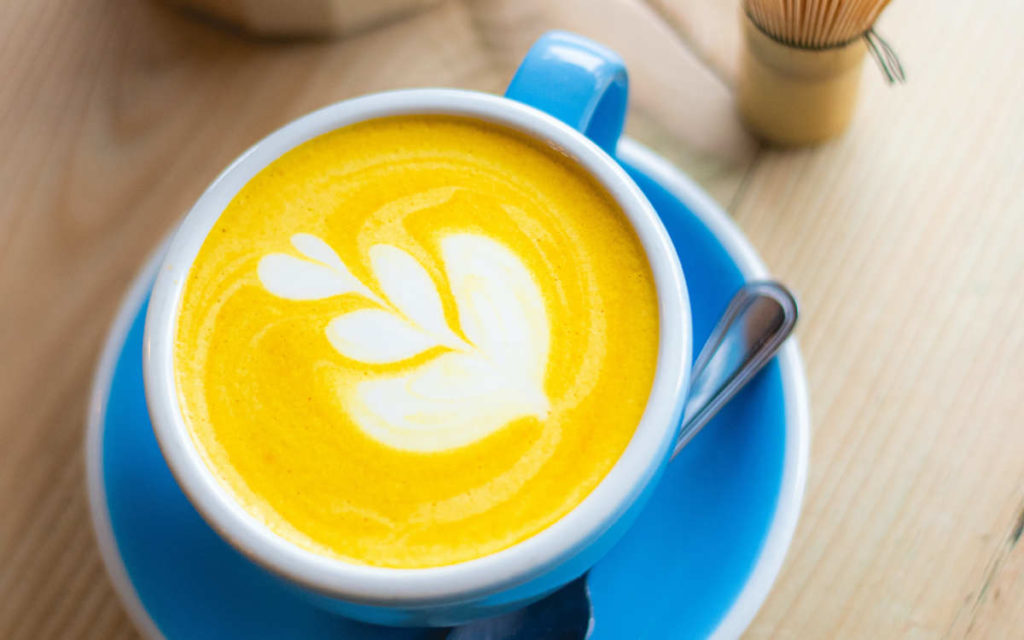 Mug with a creamy turmeric latte or golden latte on a blue saucer, great for immune support and recovery. 