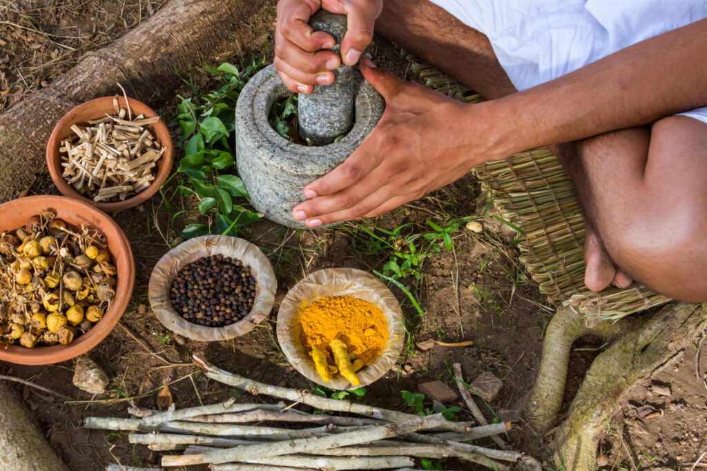 Man with mortar and pestle grinding turmeric and neem with other herbs and spices.