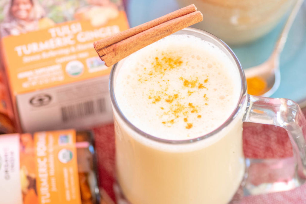 Clear hot mug filled with golden turmeric holiday latte with cinnamon stick and turmeric. 