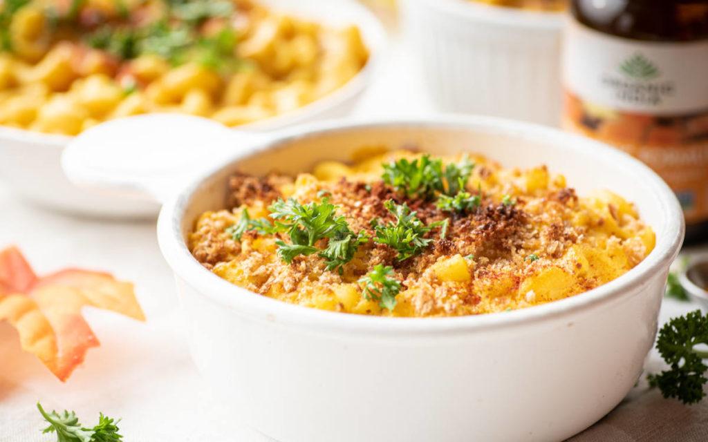 Vegan butternut mac n cheese in a white oven-safe bowl with breadcrumbs on top. 