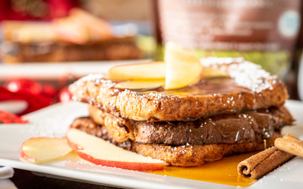 Cinnamon french toast with maple syrup and powdered sugar with cinnamon sticks and apples.