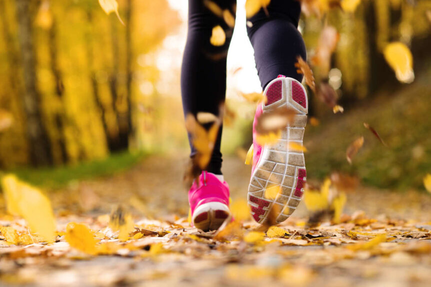 Wellness tips for runners, woman running with pink sneakers on a autumn leave-showered path.