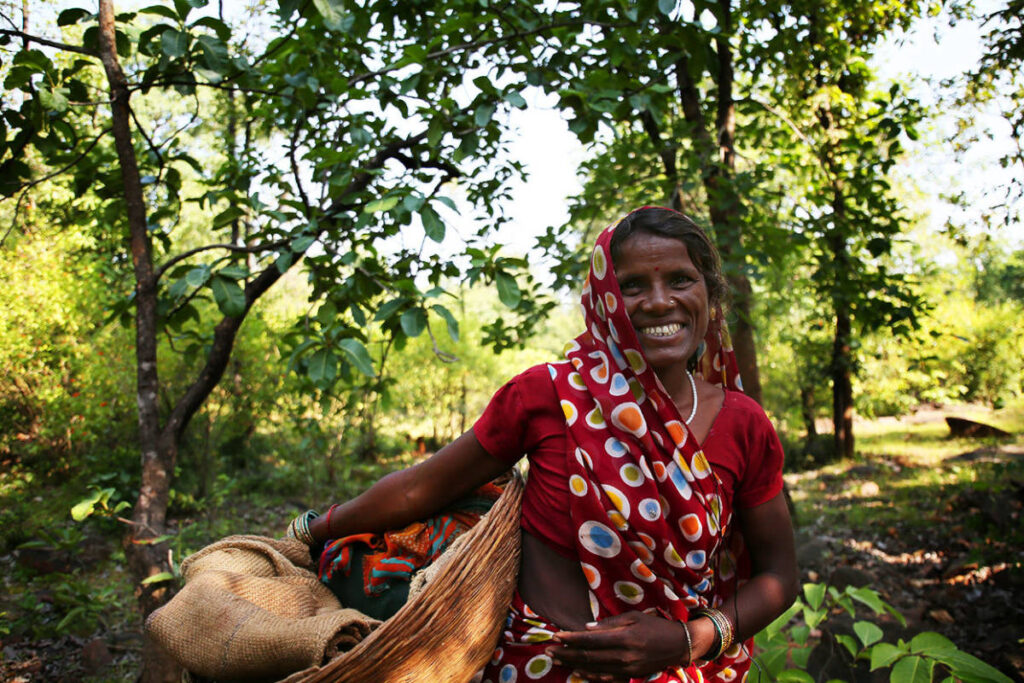 Woman wildcrafter smiling in orange sari while wildcrafting in forest. Photo by Organic India.