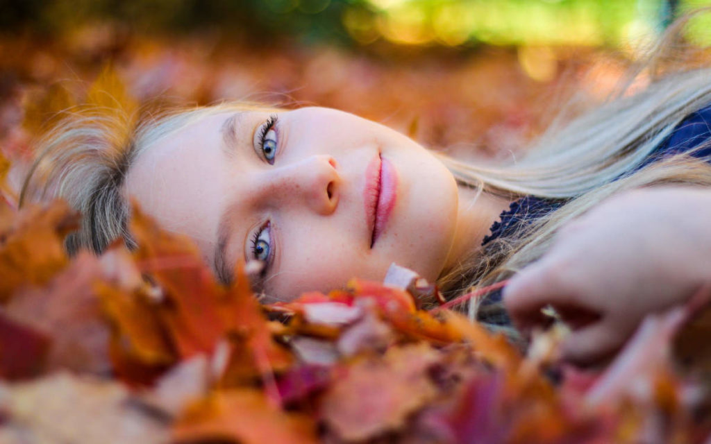 Woman blonde hair blue eyes laying in foliage during autumn, or vata season