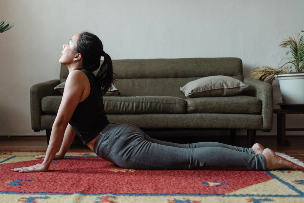 Black hair woman on carpet in living room doing cobra pose for digestion. 