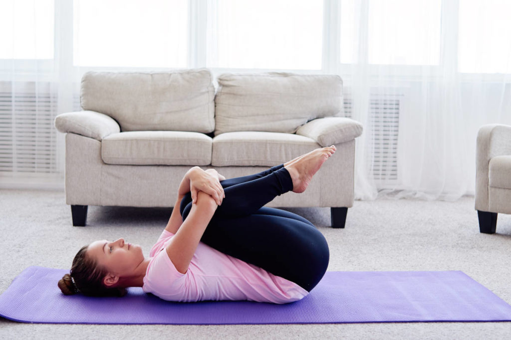 Woman on purple yoga mat in her living room doing yoga poses for digestion. 